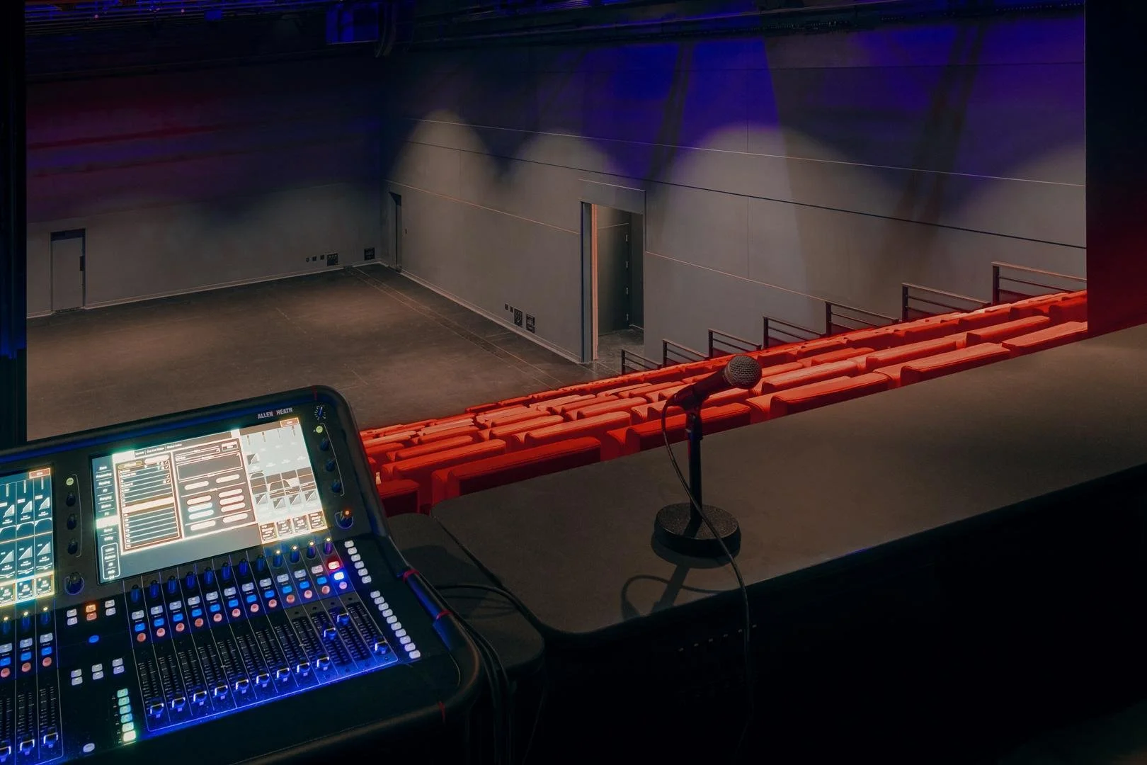 View from the technical control room showing a digital sound mixing console in the foreground overlooking the theater seating and stage.