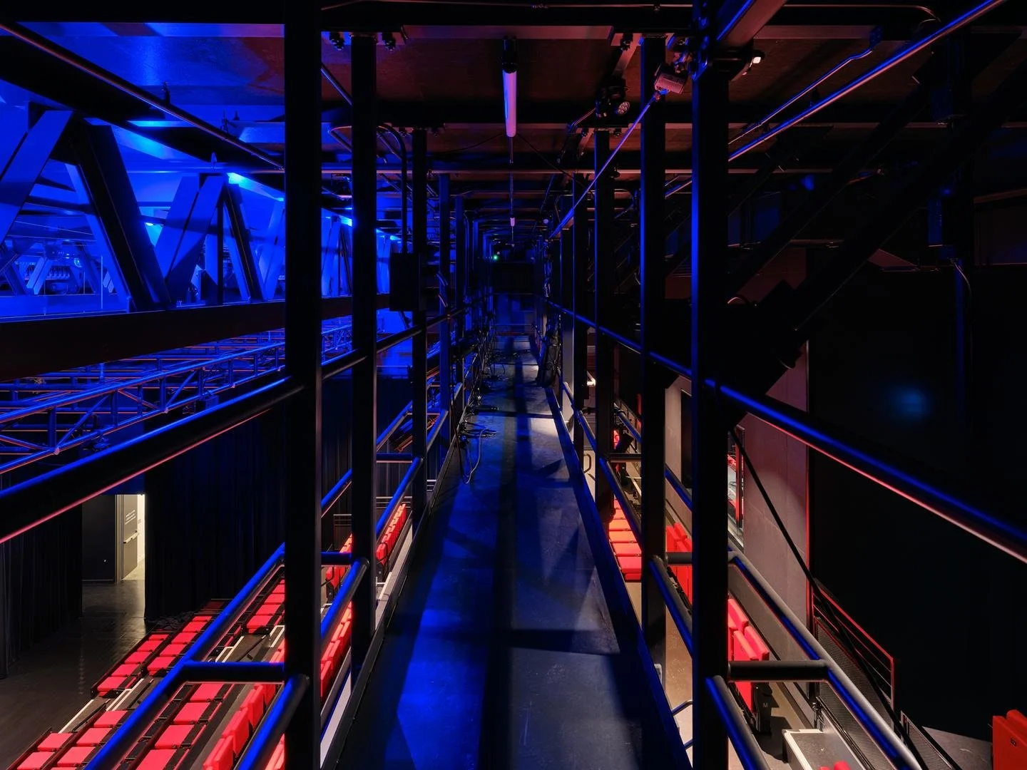 Vue vertigineuse depuis la passerelle technique du Grand Espace, plongeant vers les gradins de sièges rouges partiellement visibles sous un éclairage bleuté.