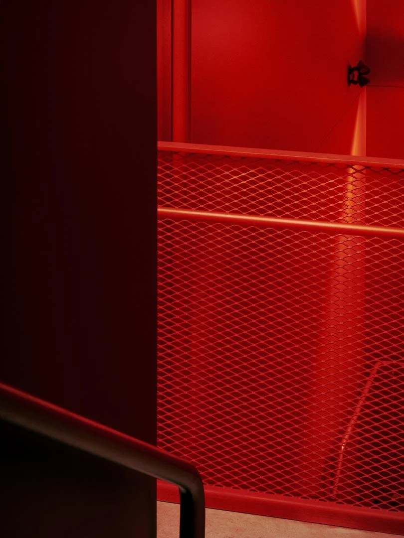 Close-up architectural detail of the red expanded metal mesh guardrail and handrail inside the vividly painted stairwell of Le Grand-Espace.