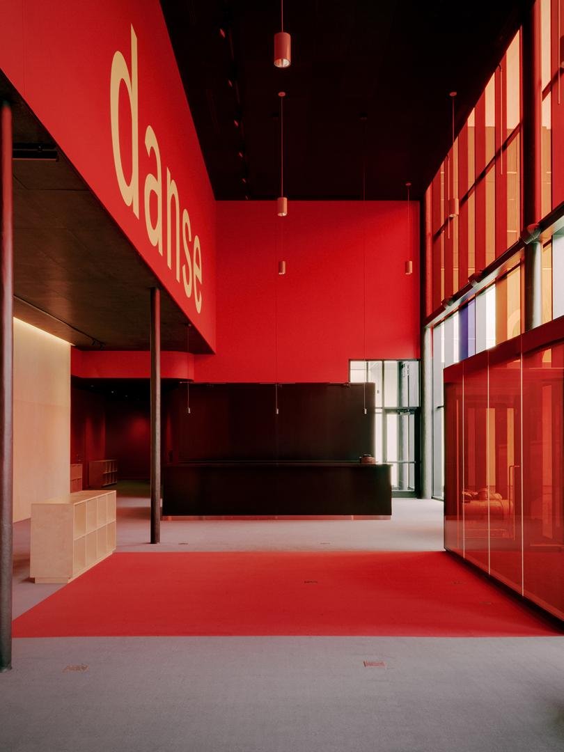 Vibrant interior of Le Grand-Espace foyer featuring a striking red wall with large yellow "danse" typography and an open black bar for drinks and food.