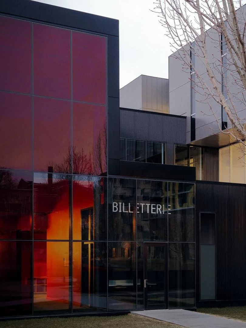 Exterior view of the transparent glass box office integrated into the black corrugated metal and red glass volumes of Le Grand-Espace.
