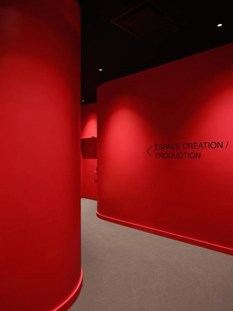 Couloir immersif aux murs courbes entièrement peints en rouge vif, avec une signalétique minimaliste noire indiquant l'Espace Création / Production.