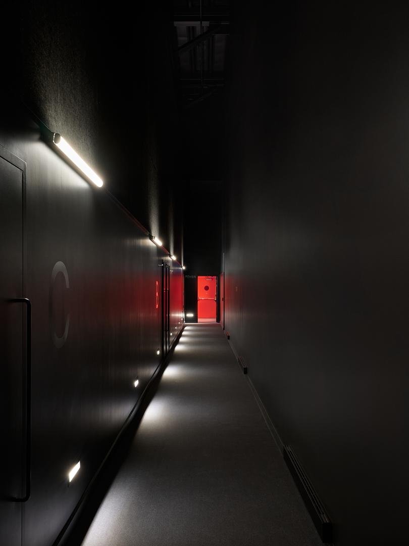Corridor monumental formant le sas acoustique du Grand Espace de Sherbrooke, avec un éclairage dramatique menant du foyer rouge vers les portes de la salle.