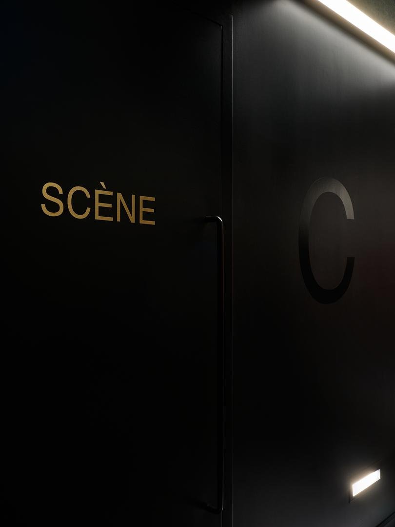 Détail de la signalétique minimaliste du Grand Espace de Sherbrooke : le mot SCÈNE en lettres dorées sur une porte noire mate.