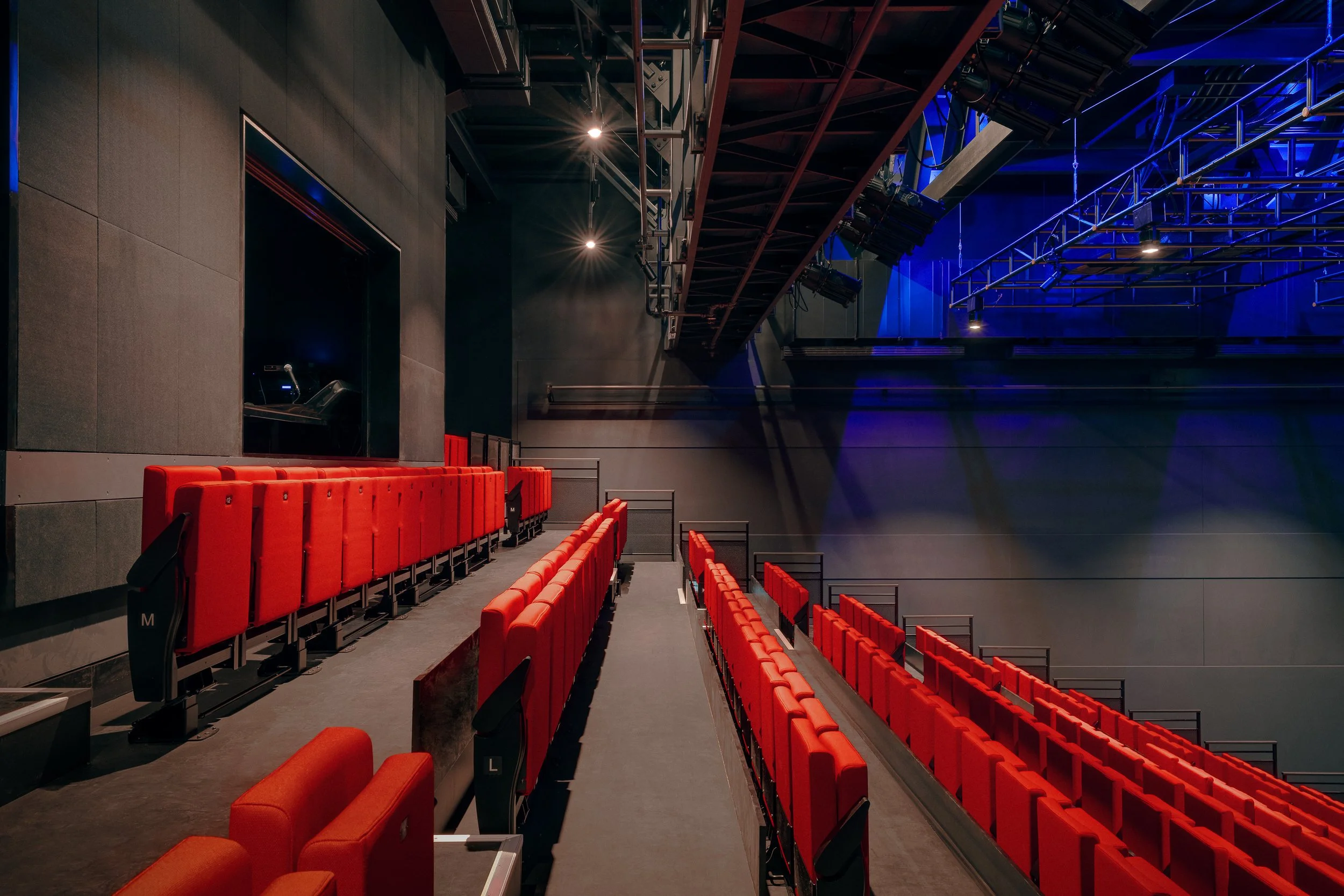Elevated side view looking down the rows of bright red theater seats demonstrating the steep rake of the motorized seating system.