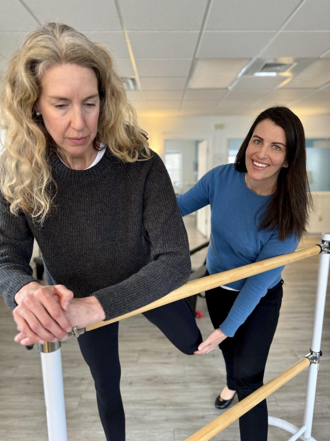 female brunette physical therapist helps a blonde female patient lift her knee
