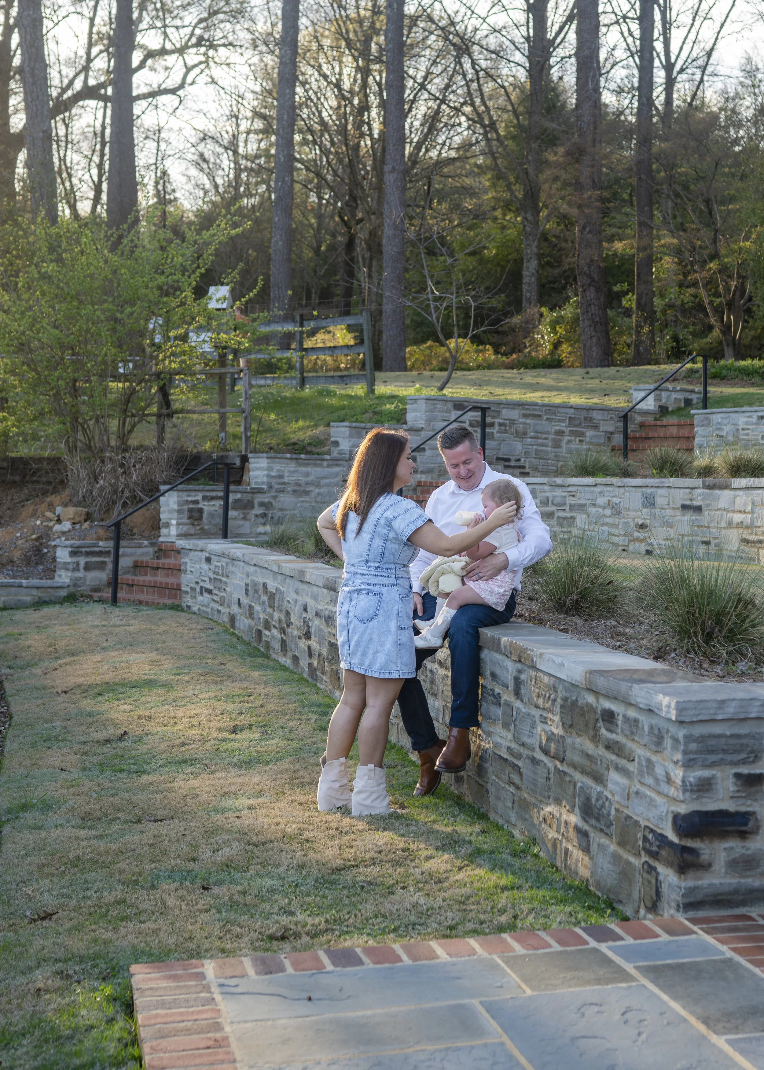 family of 3 at the botanical gardens with dad giving toddler a bottle. Family photoshoot at the Birmingham Botanical Gardens