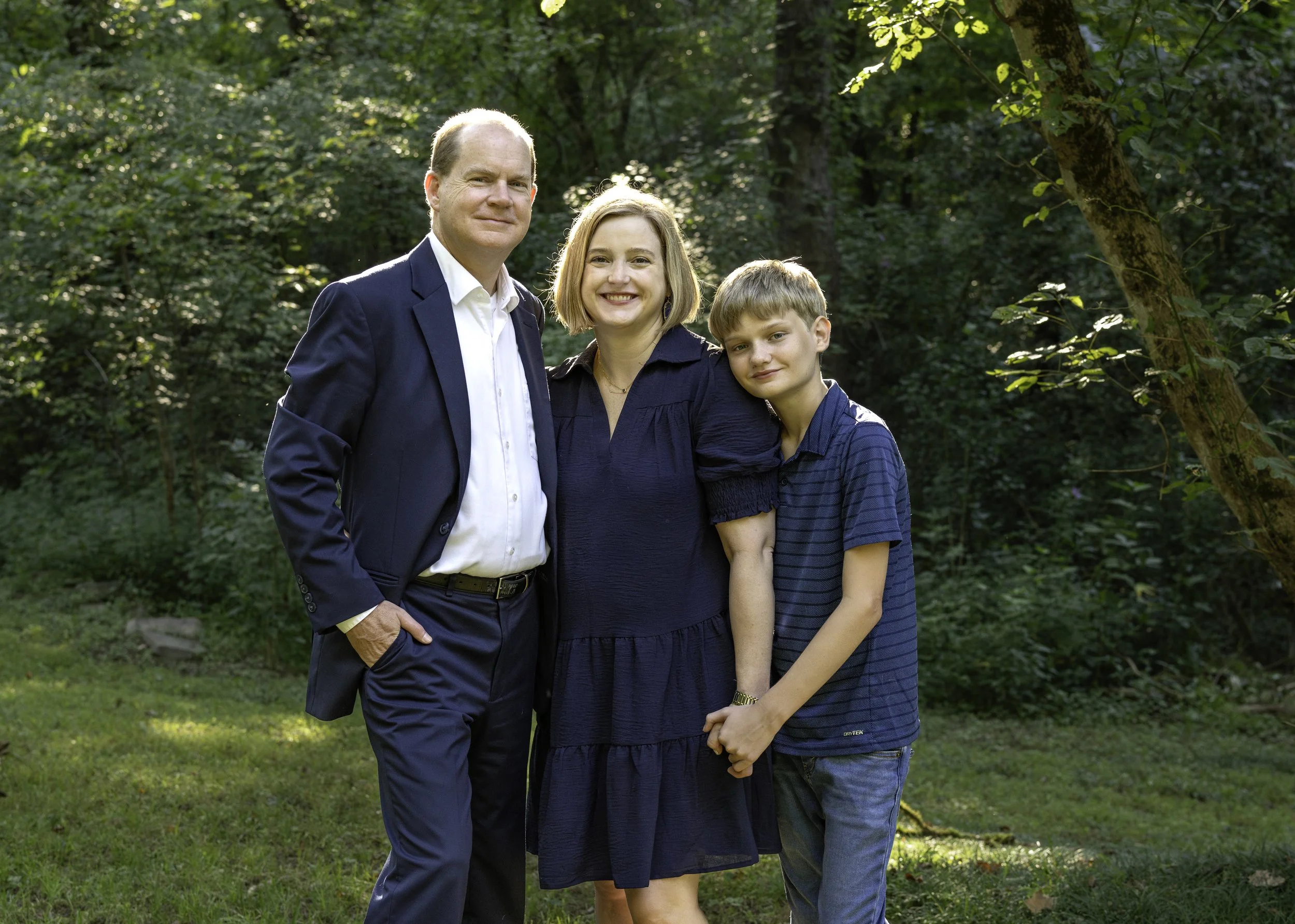 family of 3 standing in front of trees