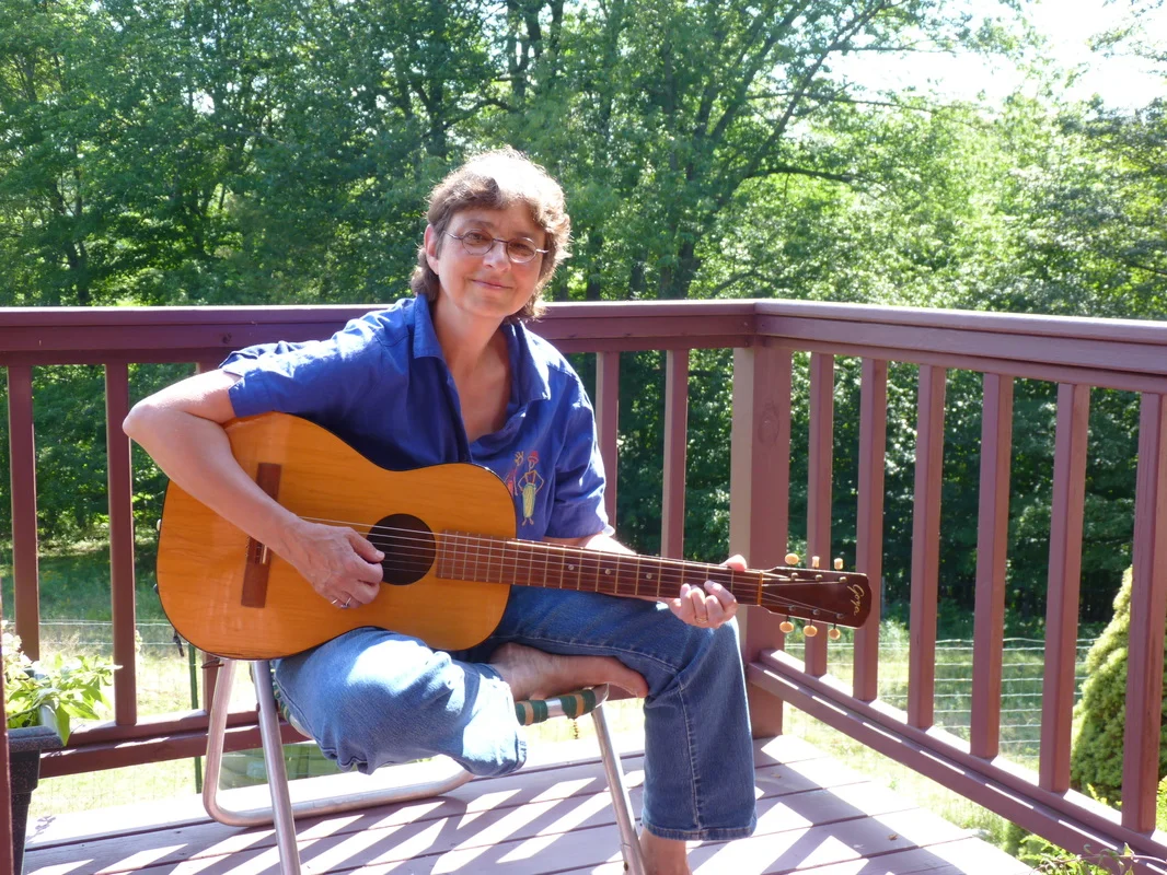 A woman playing guitar on a porch in front of the railing