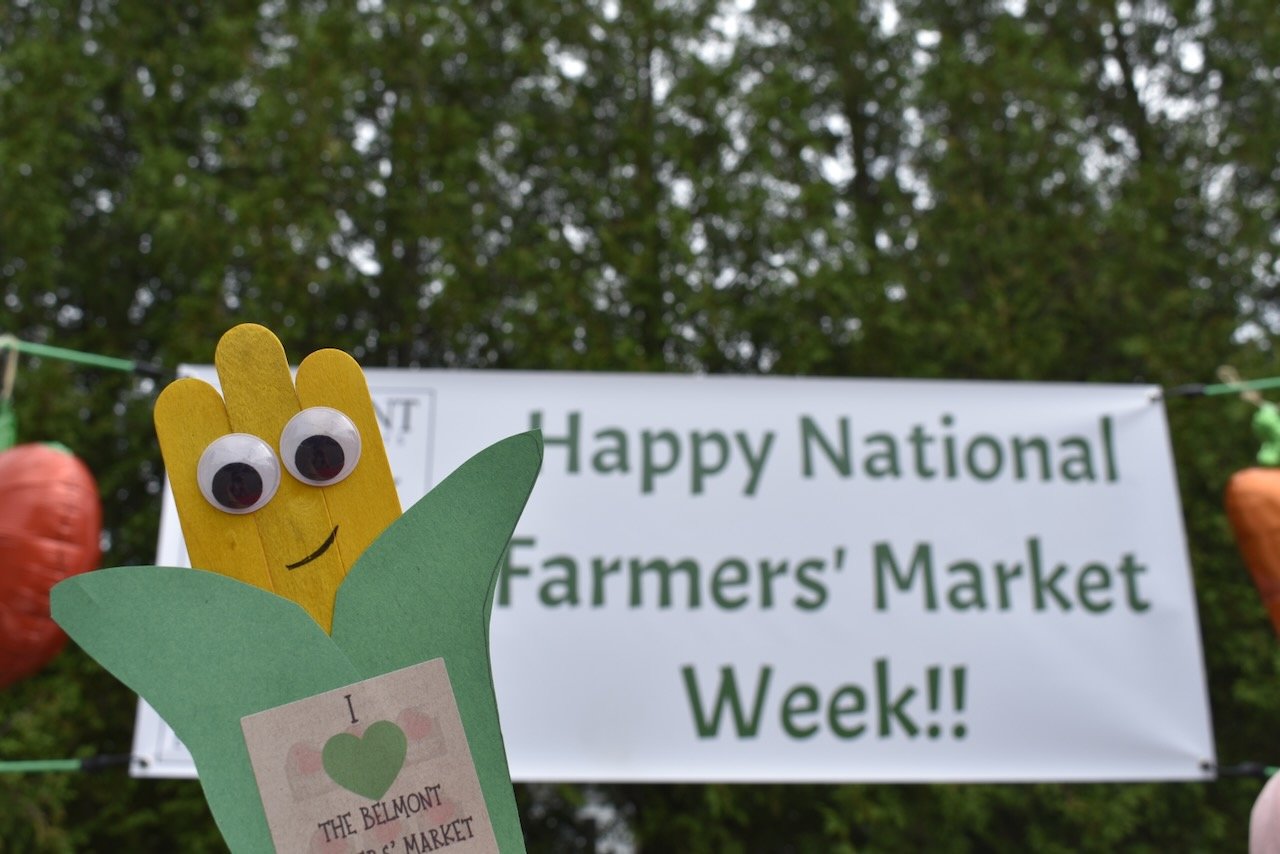 A  sign that says "Happy National Farmers Market Week!" with an image of an ear of corn