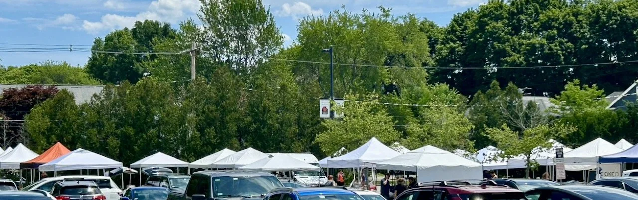 blue sky, green trees, a collection of tent tops in the market and cars in the lot