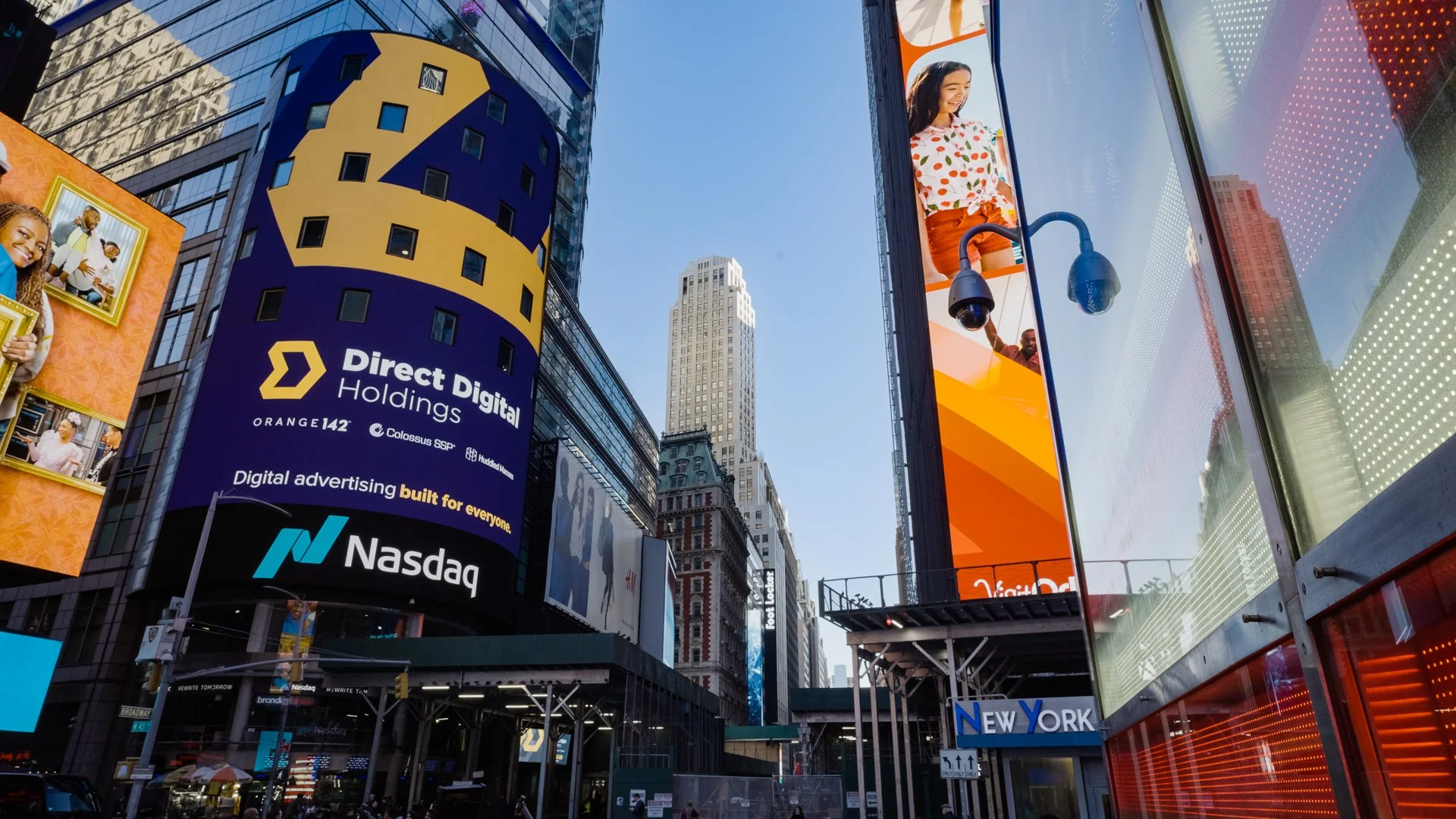 Time Square, New York City with electronic billboards and tall buildings, including a large Nasdaq sign, digital advertising, and people walking below.