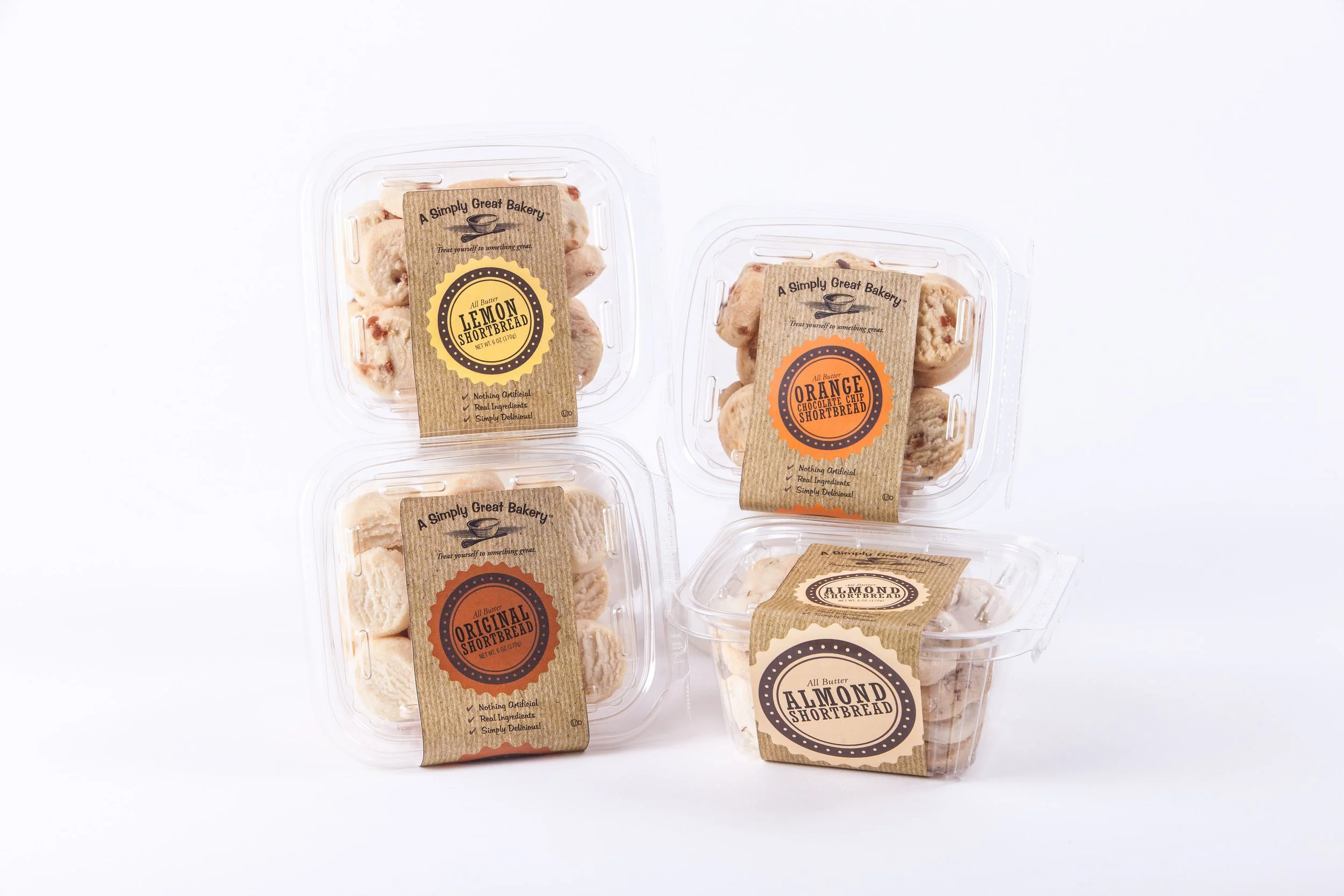 Four containers of shortbread cookies with brown paper labels displaying various flavors like lemon, orange, original, and almond on a white background.
