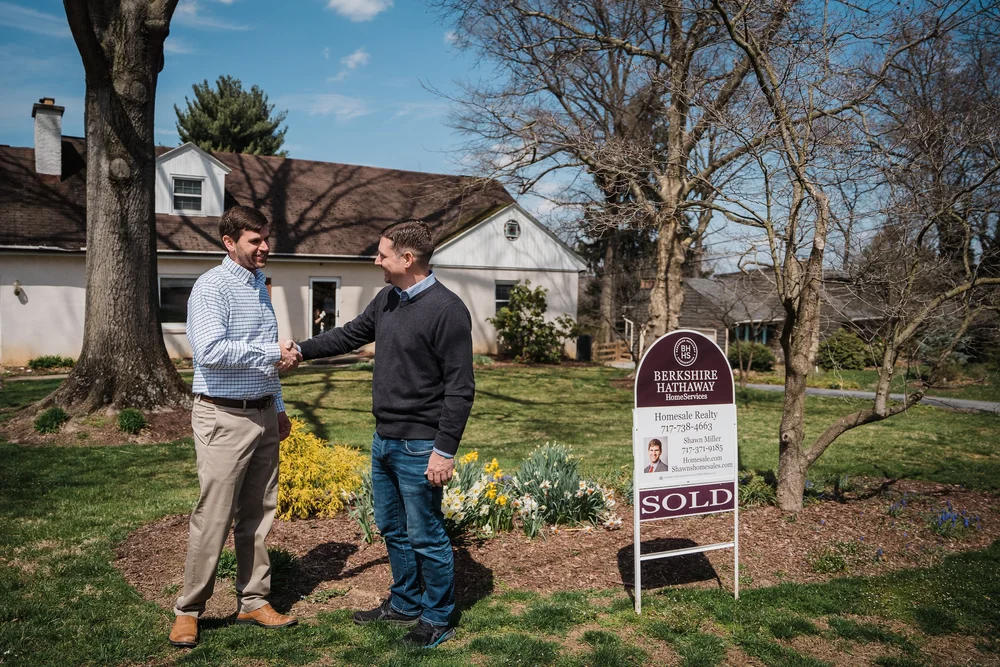 Shawn Miller meeting a client beside a sold sign outside a home