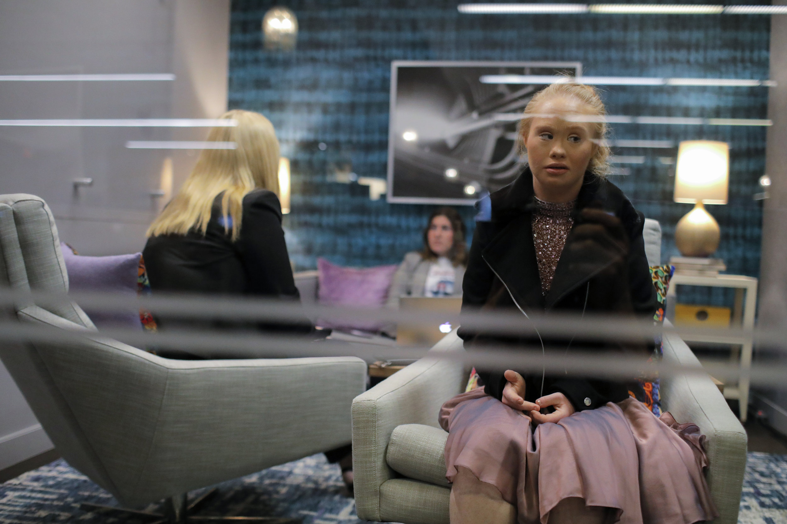  Madeline looks through a window as her mother is interviewed by a reporter at the Huff Post. Madeline has incredibly limited vocabulary and her mother typically takes care of the verbal side of media interactions.  