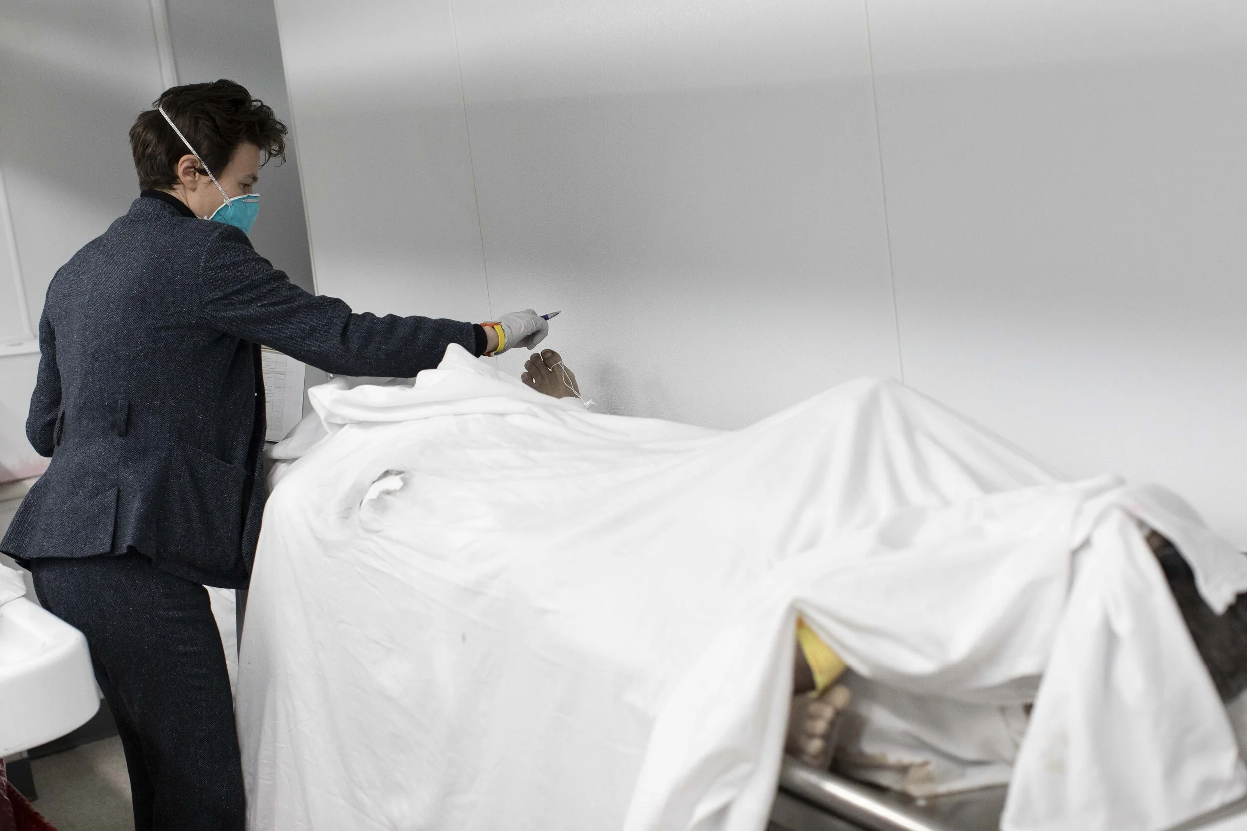  Lily Sage Weinrieb checks the identification of a body in the funeral home’s basement. With space in short supply, bodies shared stretchers top-to-tail.  