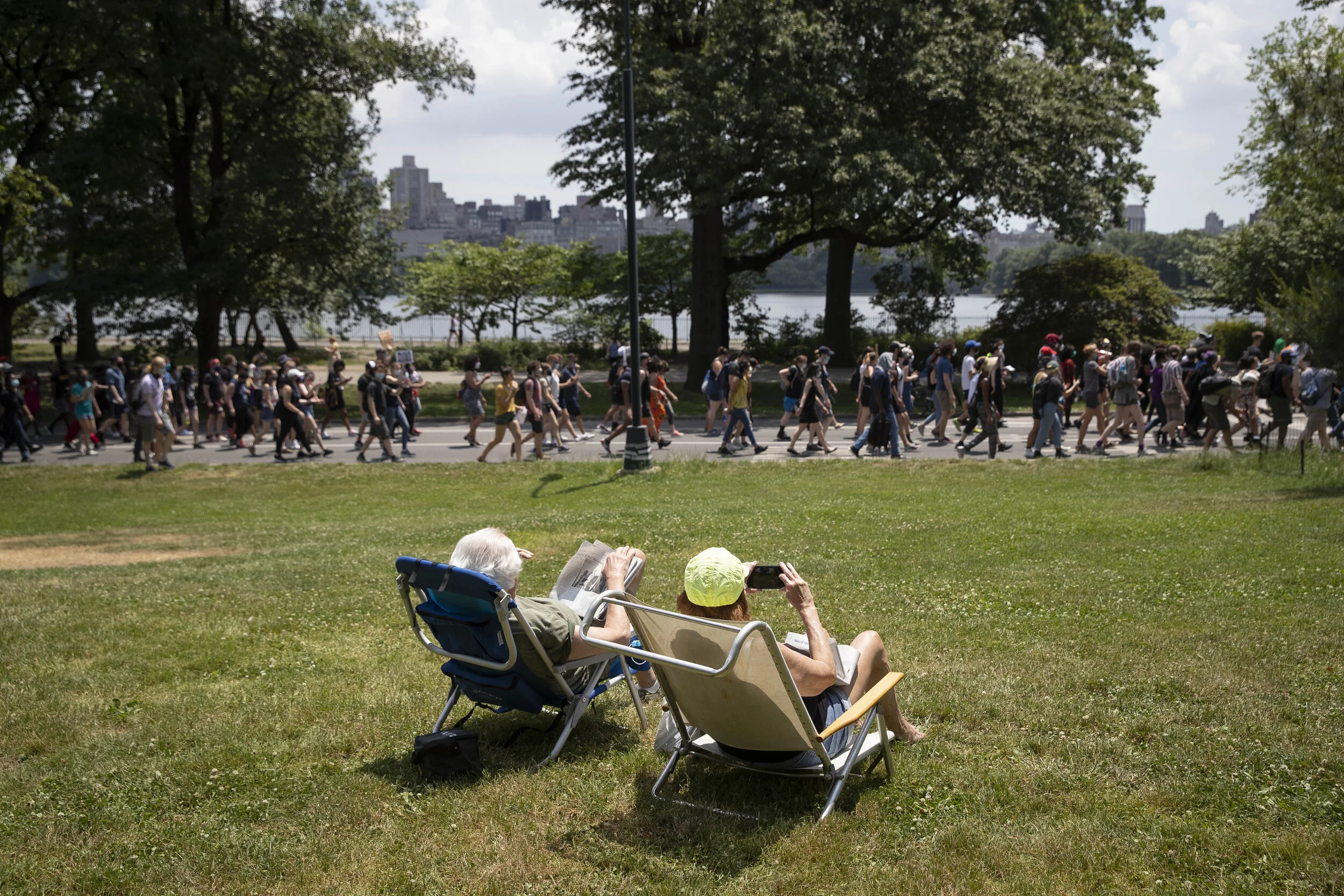  People in sun chairs watch on as protesters march through Central Park on the Juneteenth holiday.  