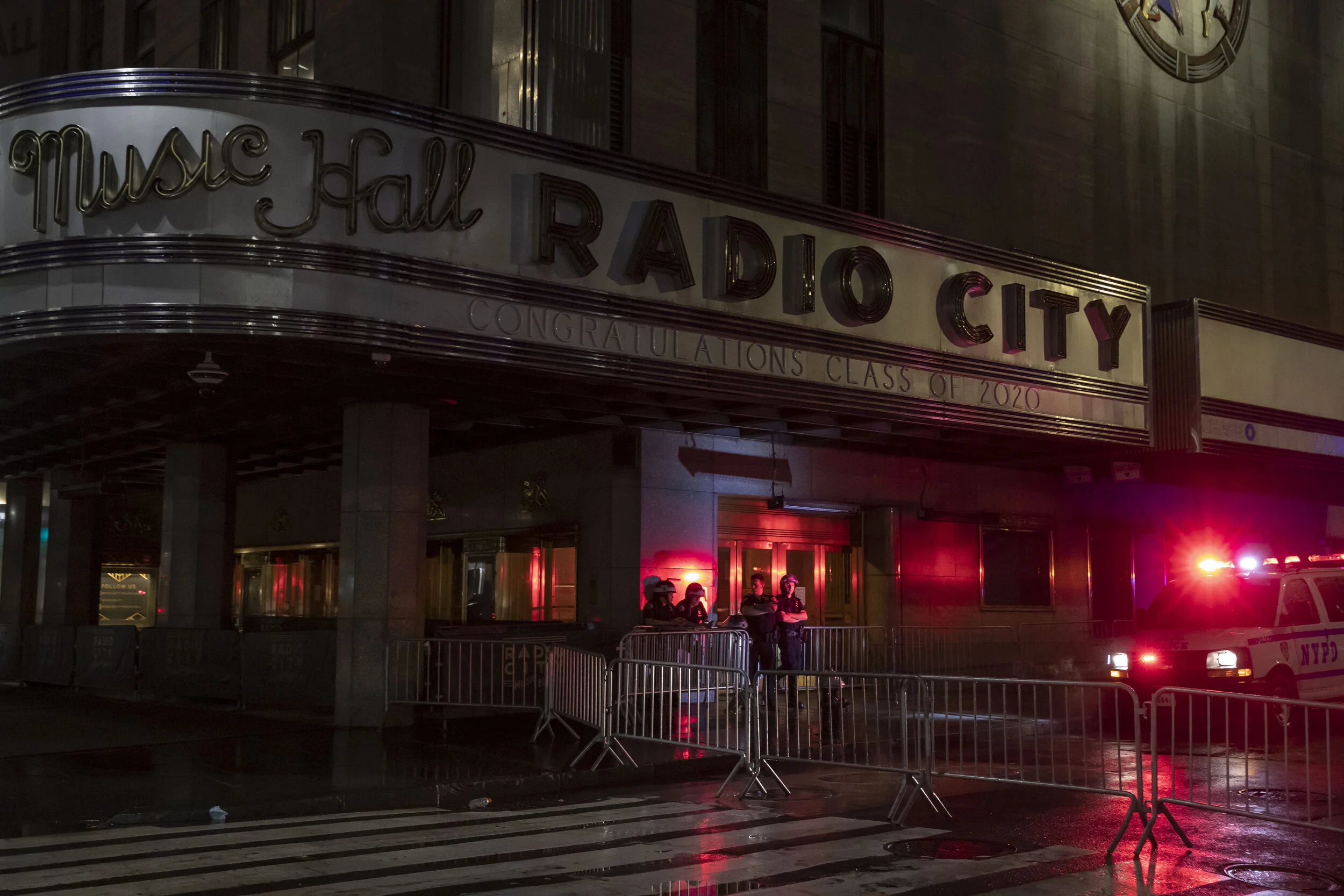  New York Police Department officers stand under the awning of Radio City Music Hall after the 8:00 PM curfew put in place to attempt to curb night time looting that was occurring during protests in New York City.  