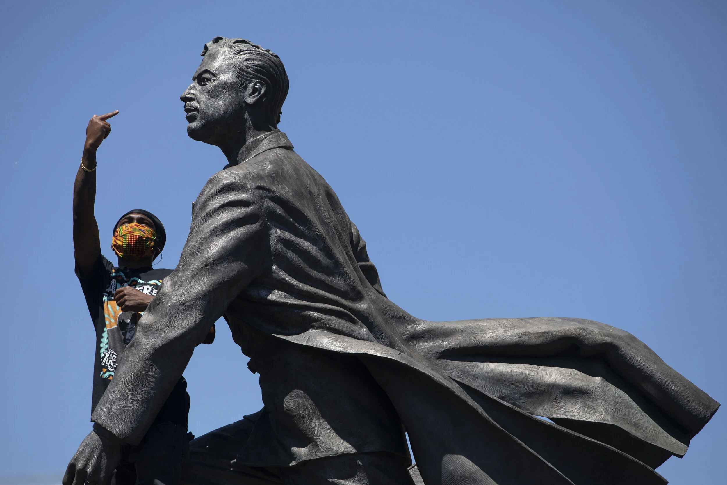  A protester gestures toward a police helicopter above as he stands on a statue of African-American pastor and politician Adam Clayton Powell Jr. in Harlem, New York City.  