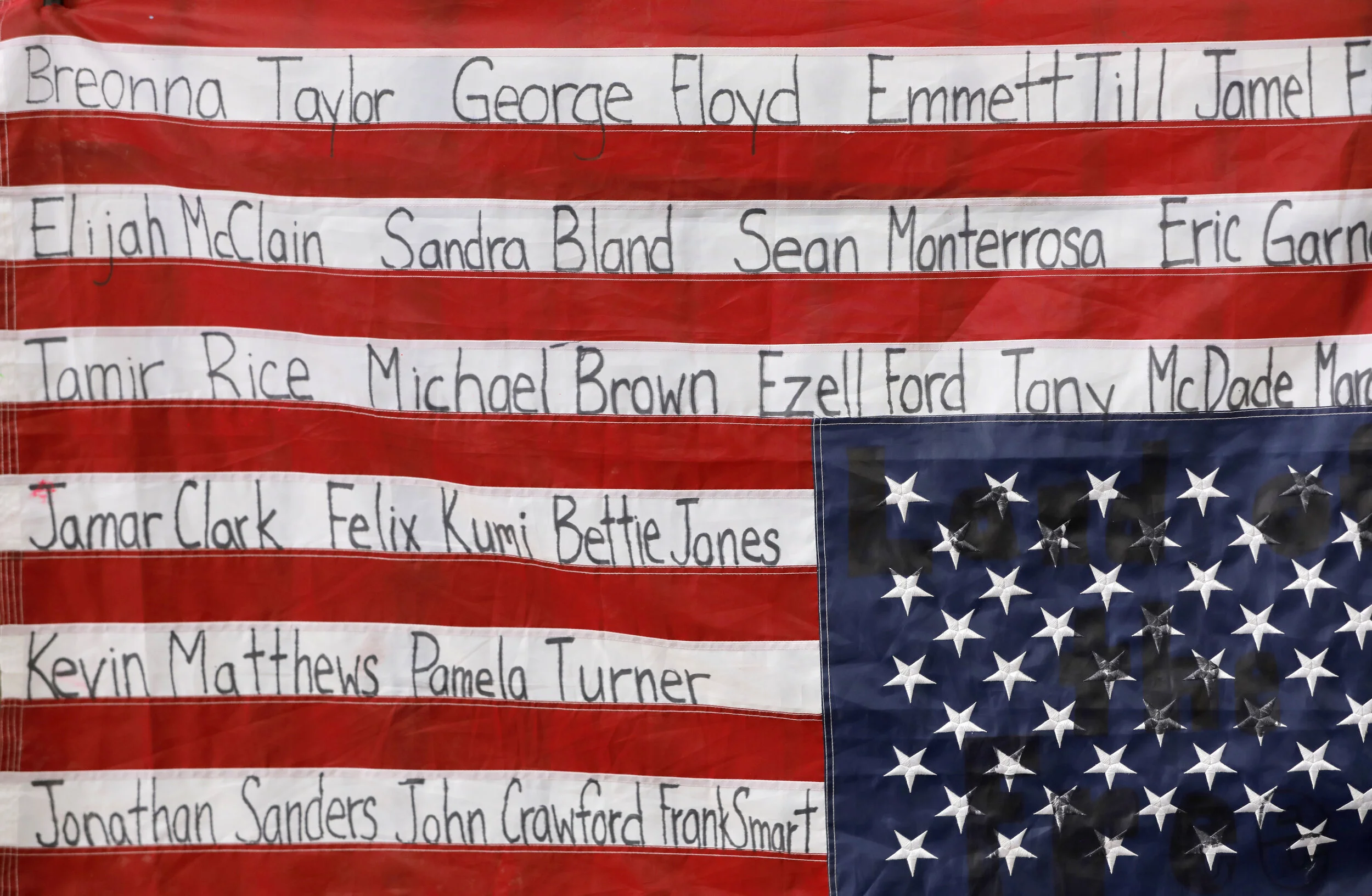  The names of black people killed by police is seen written on an upside down flag of the United States.  