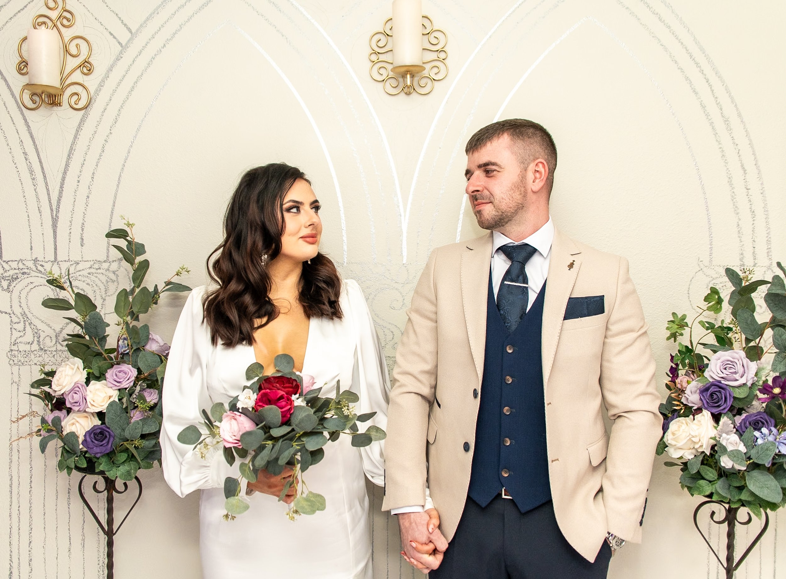 Young couple looking into each others eyes while holding hands agains a painted archway