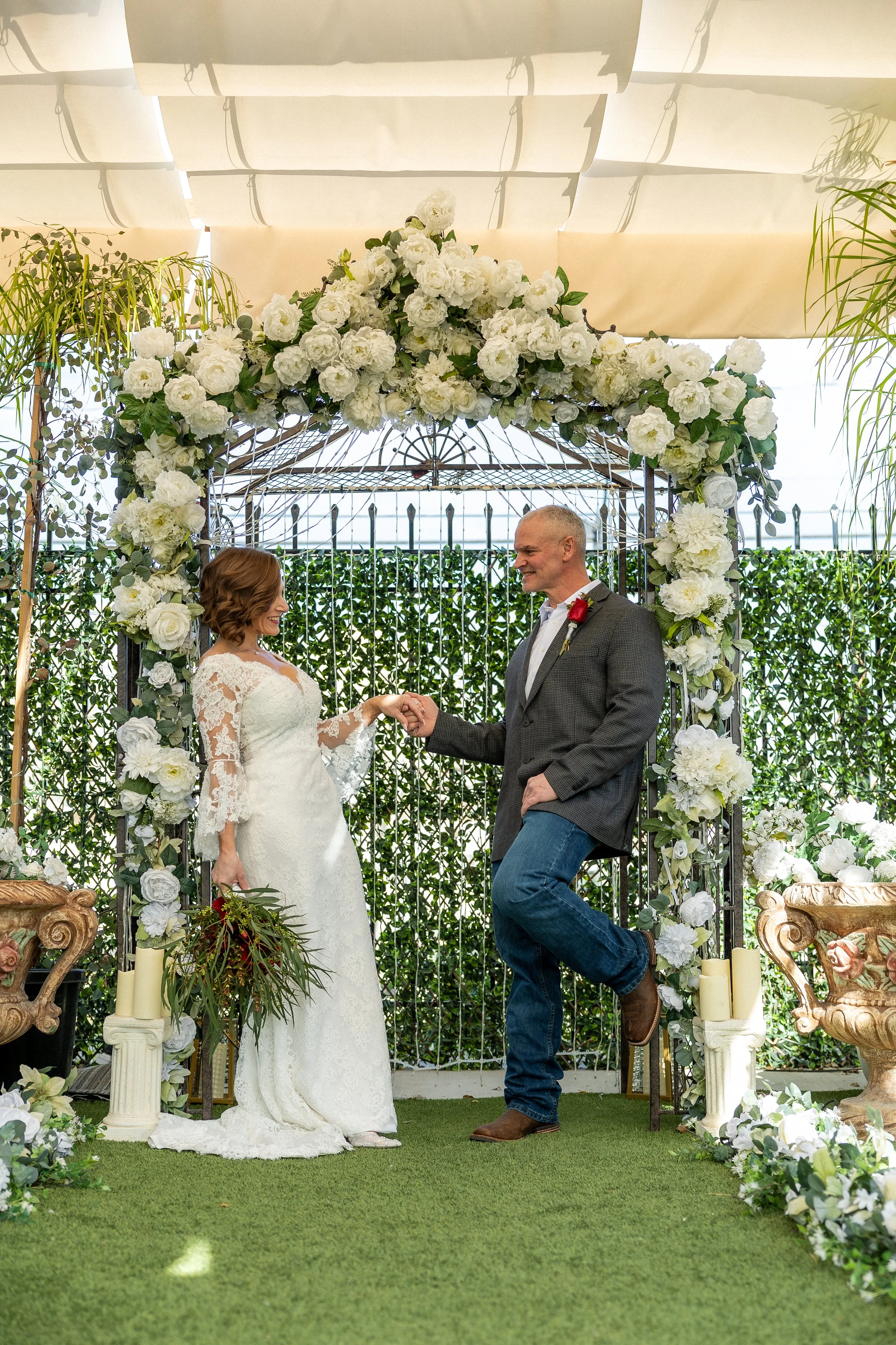 Couple leaning against a floral drenched altar gazing into each others eyes surrounded by a green garden