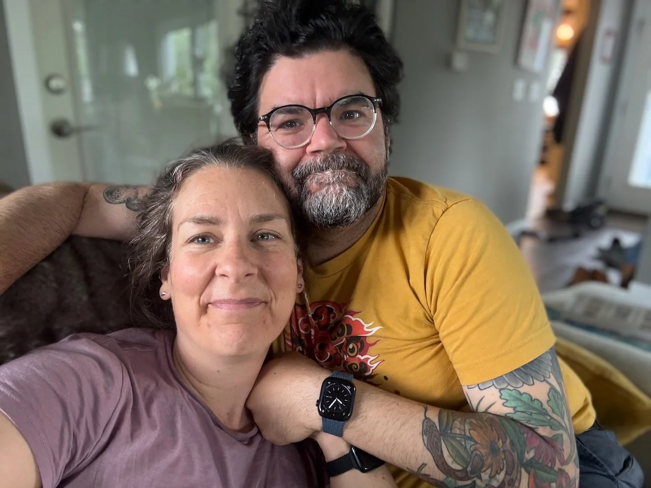 Laura Bergus and Nick Bergus sit on a couch, holding hands and smiling.
