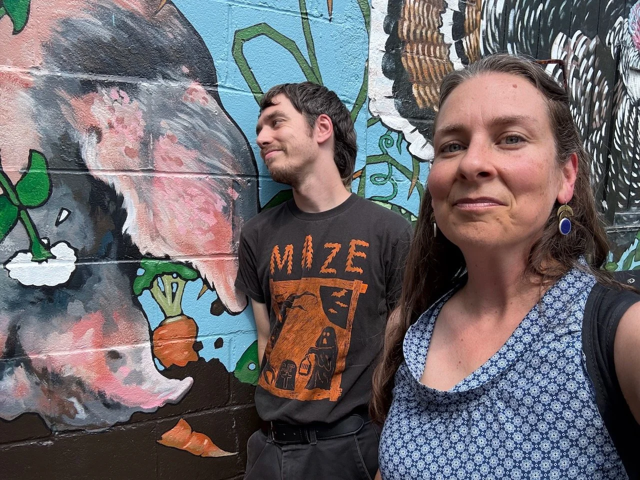 Oliver Weilein and Laura Bergus pose for a selfie in front of a mural featuring a pig and carrots.