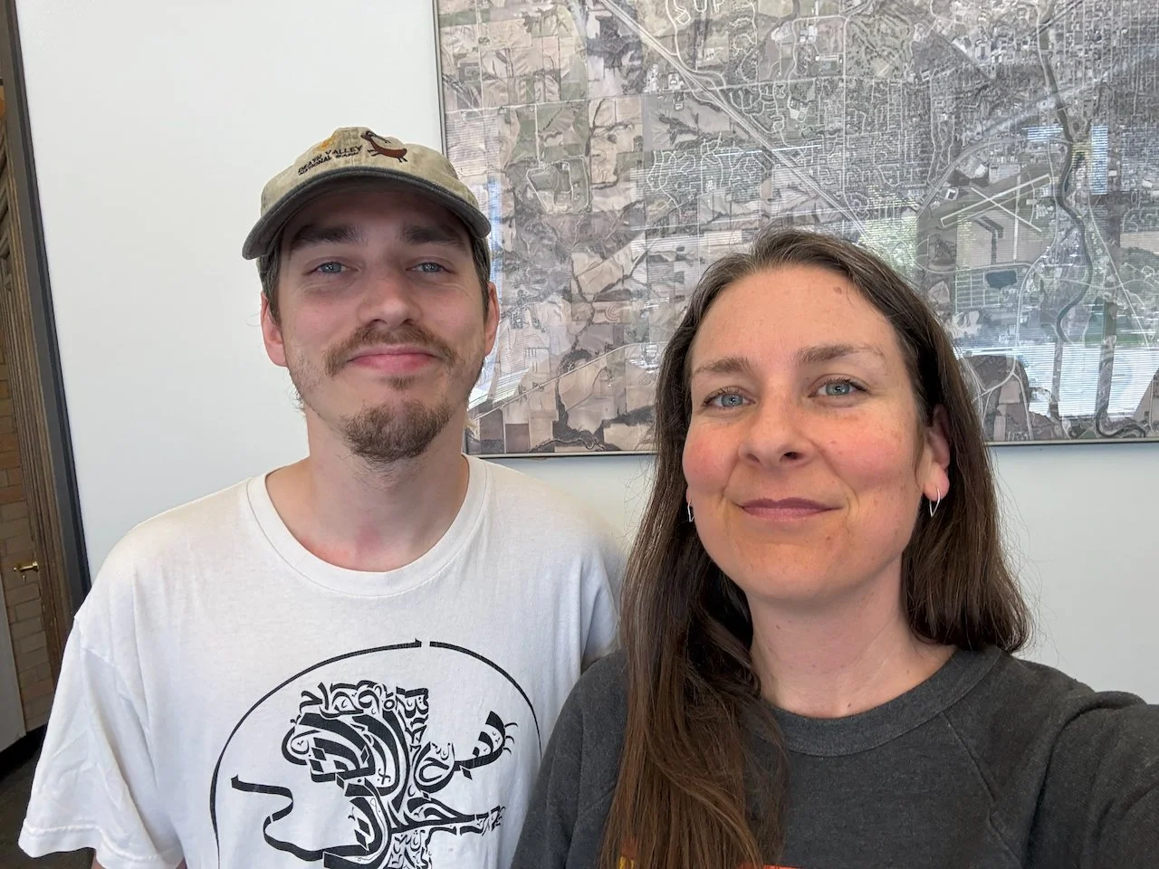 A photograph of Oliver Weilein and Laura Bergus standing in front of a map of Iowa City.