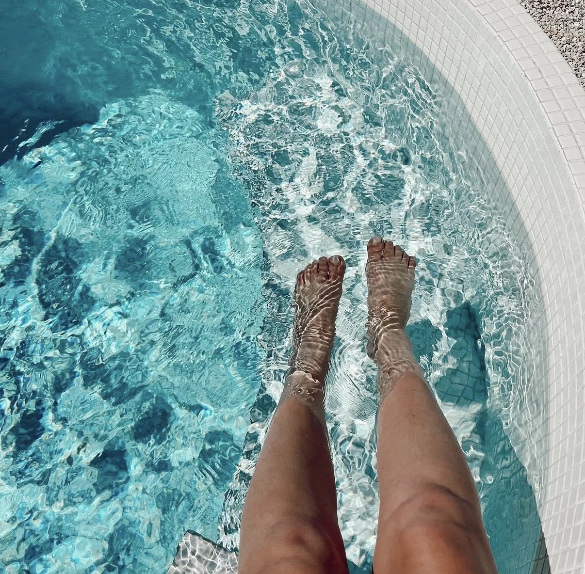 Feet submerged in a swimming pool near a white tiled edge.