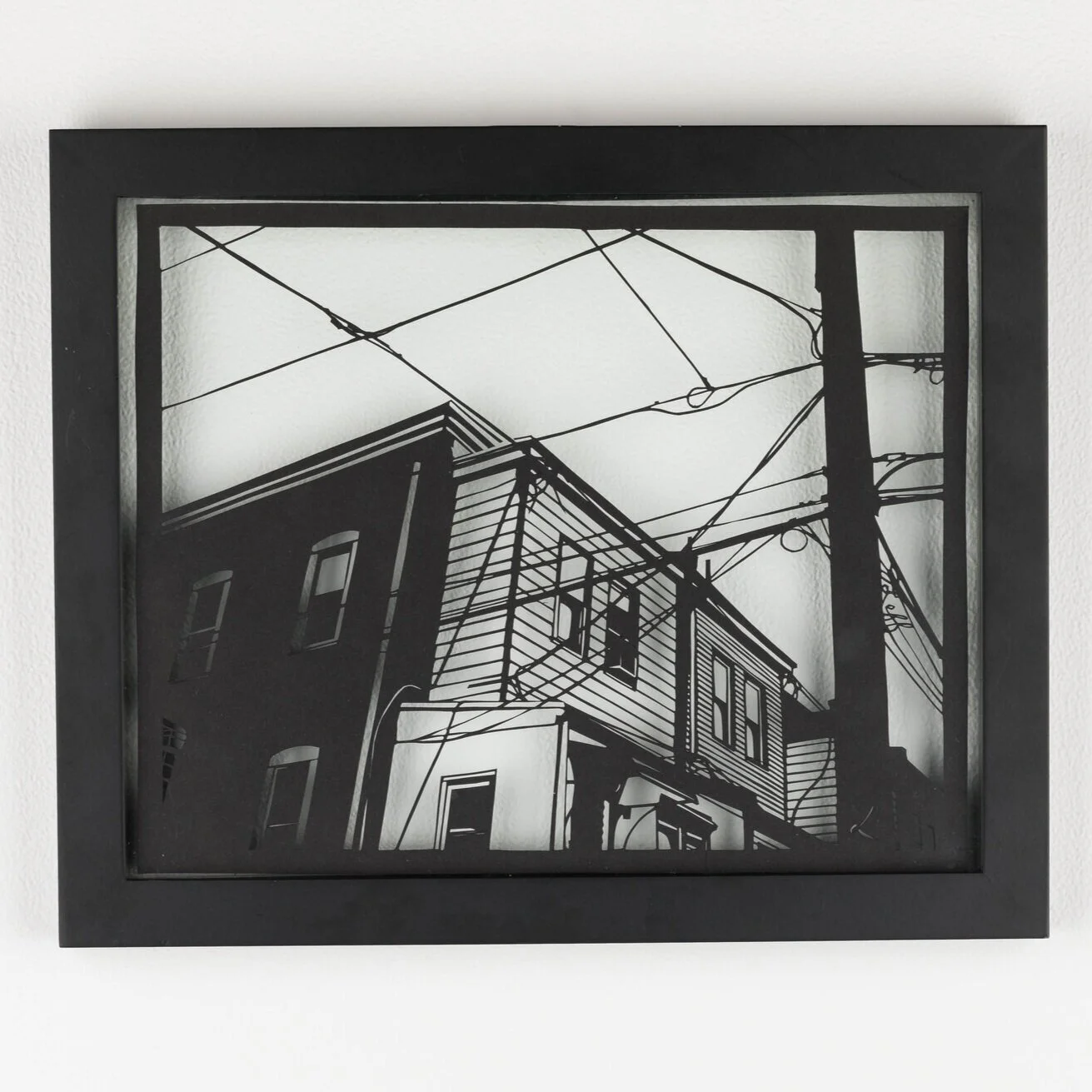 Handcut paper artwork featuring urban scene of buildings and telephone wires by Rosa Leff in floating frame