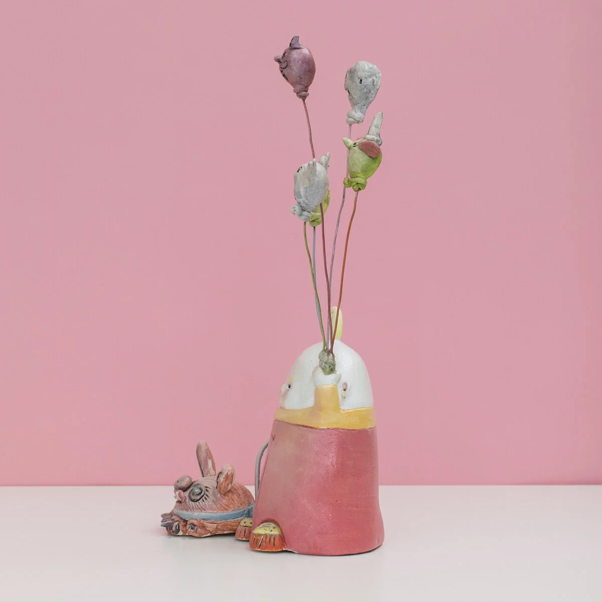 Colorful and hand built ceramic sculpture of a child with a leashed dog holding a number of balloons on strings with monster faces by Jennifer McCandless for Soapbox Arts