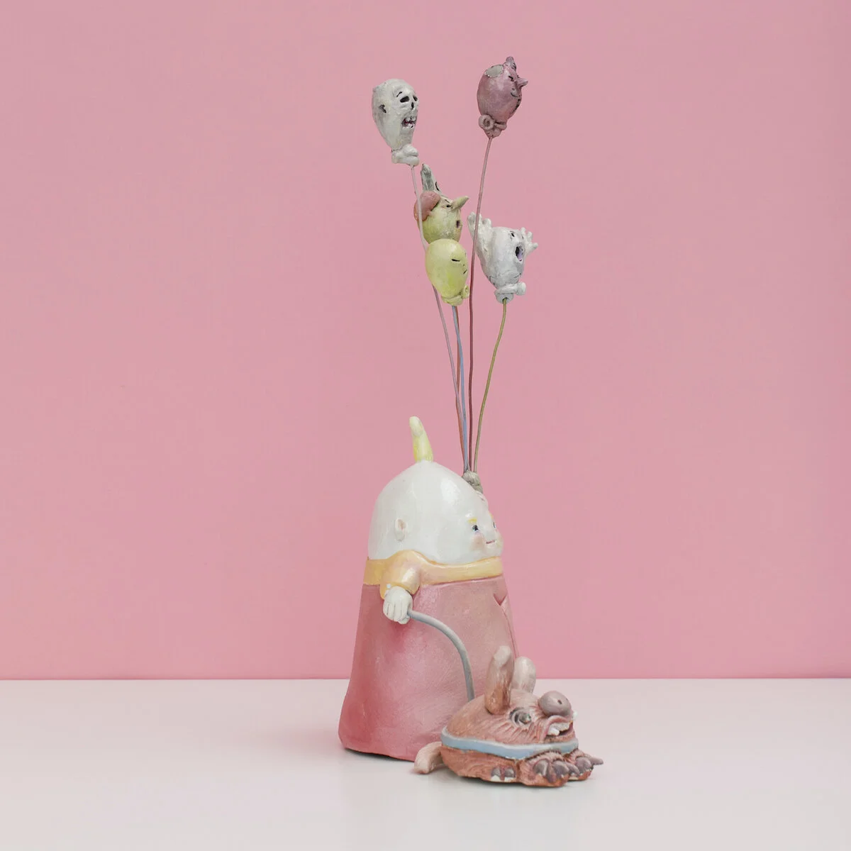 Colorful and hand built ceramic sculpture of a child with a leashed dog holding a number of balloons on strings with monster faces by Jennifer McCandless for Soapbox Arts