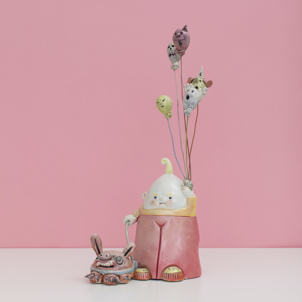 Colorful and hand built ceramic sculpture of a child with a leashed dog holding a number of balloons on strings with monster faces by Jennifer McCandless for Soapbox Arts