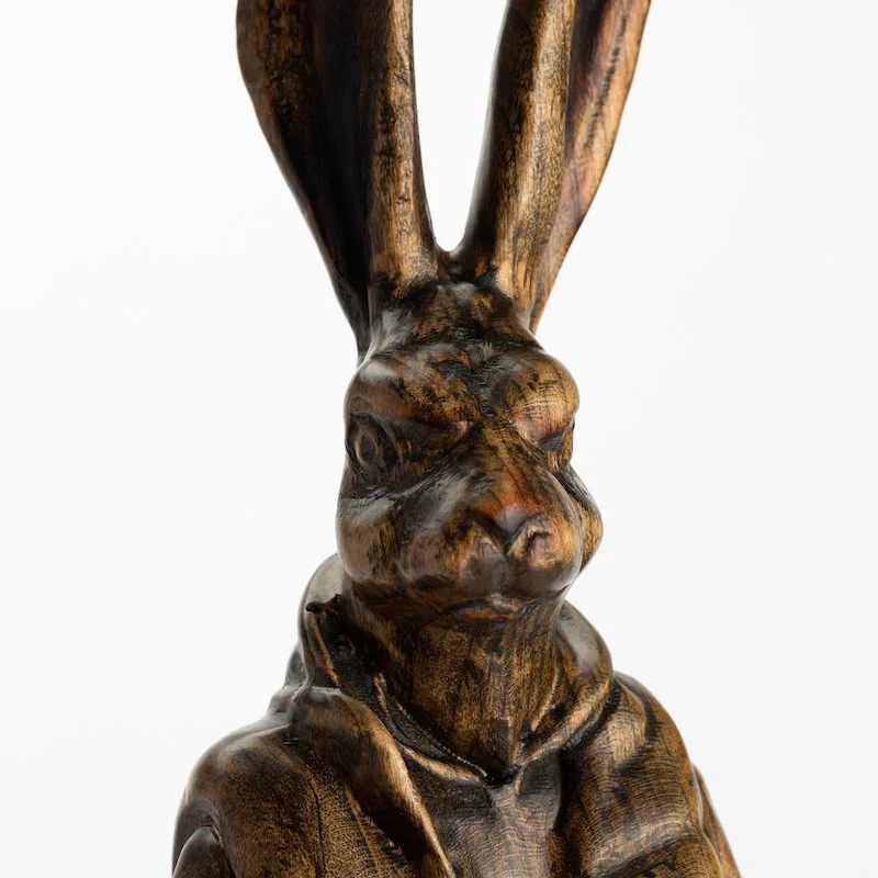 Original anthropomorphic sculpture in stained wood on a stone base of a hare wearing a puffy vest and jeans by Vermont artist and sculptor, Joe Lupiani, available @ Soapbox Arts Gallery in Vermont