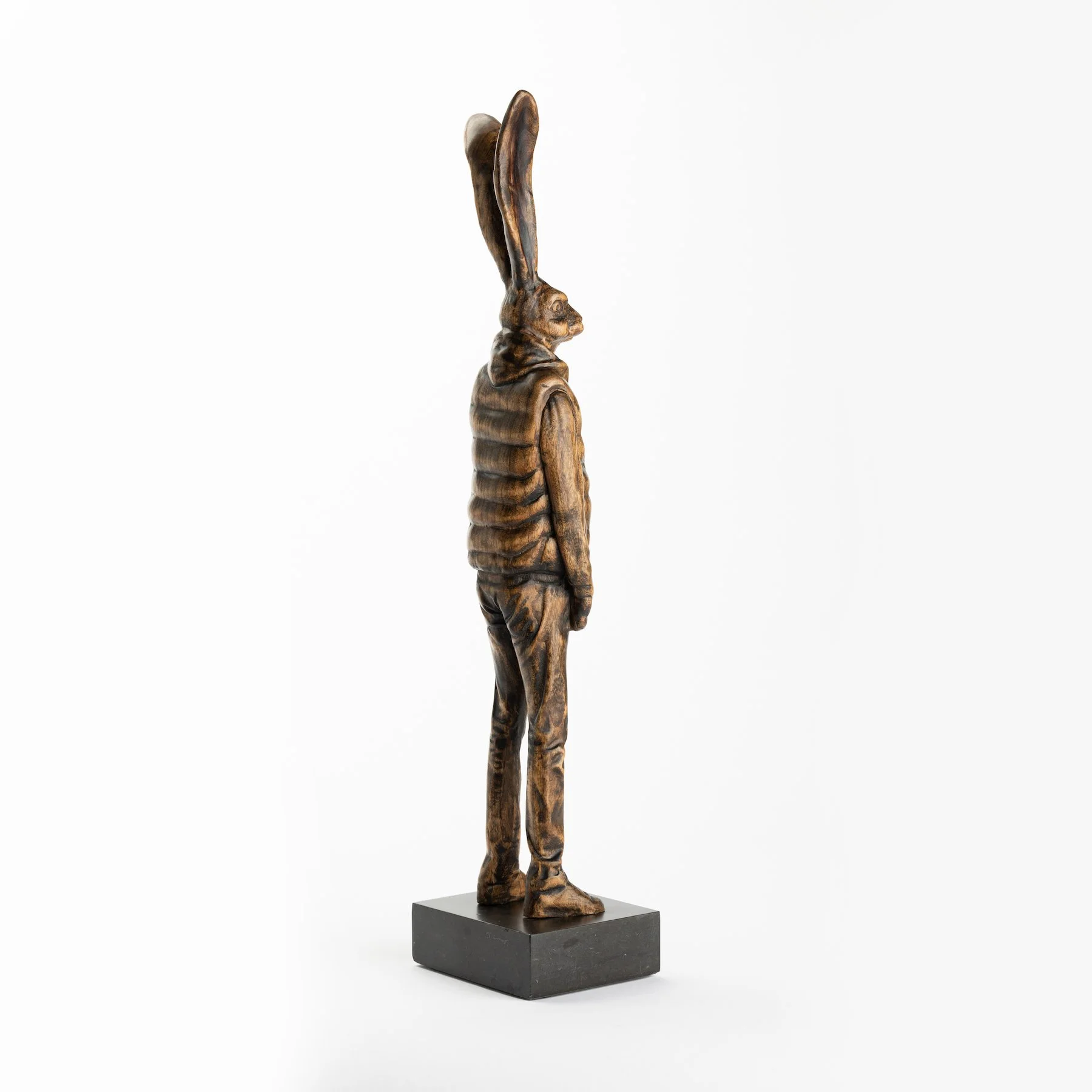 Original anthropomorphic sculpture in stained wood on a stone base of a hare wearing a puffy vest and jeans by Vermont artist and sculptor, Joe Lupiani, available @ Soapbox Arts Gallery in Vermont