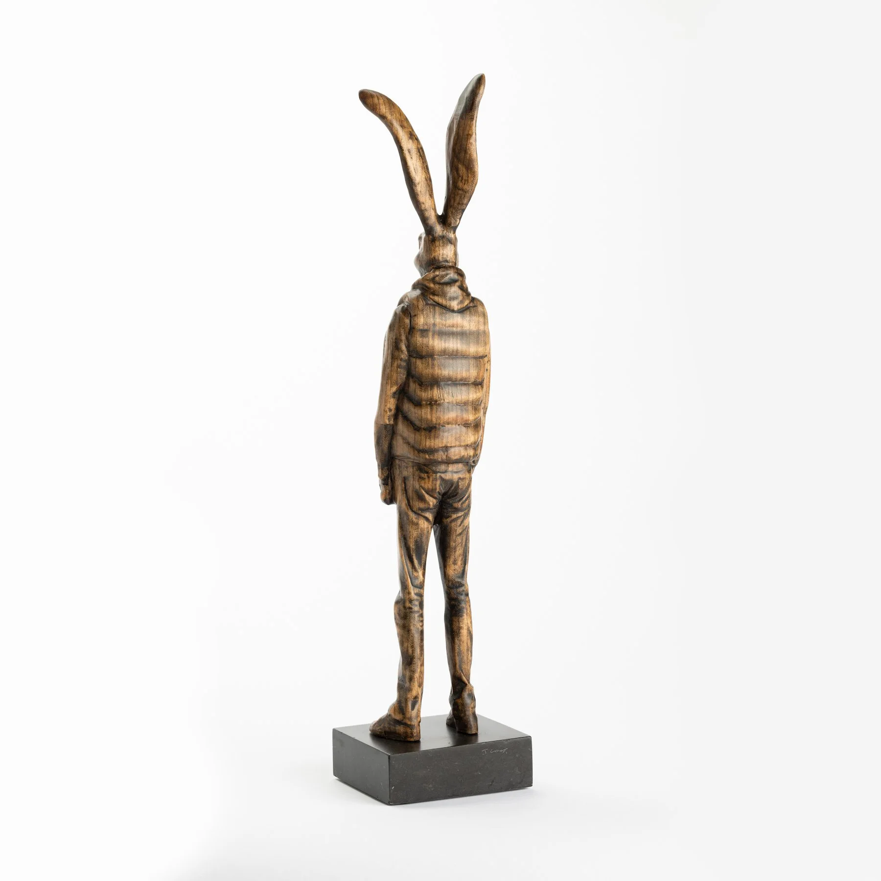 Original anthropomorphic sculpture in stained wood on a stone base of a hare wearing a puffy vest and jeans by Vermont artist and sculptor, Joe Lupiani, available @ Soapbox Arts Gallery in Vermont