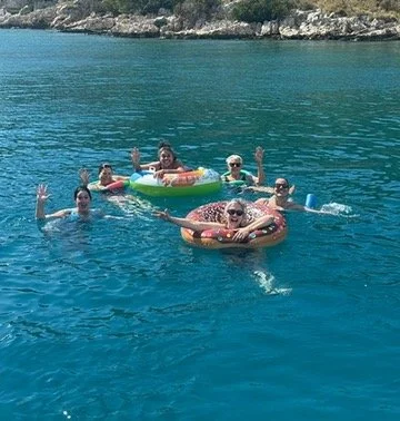 people in the sea waving at the camera whilst floating in floaties