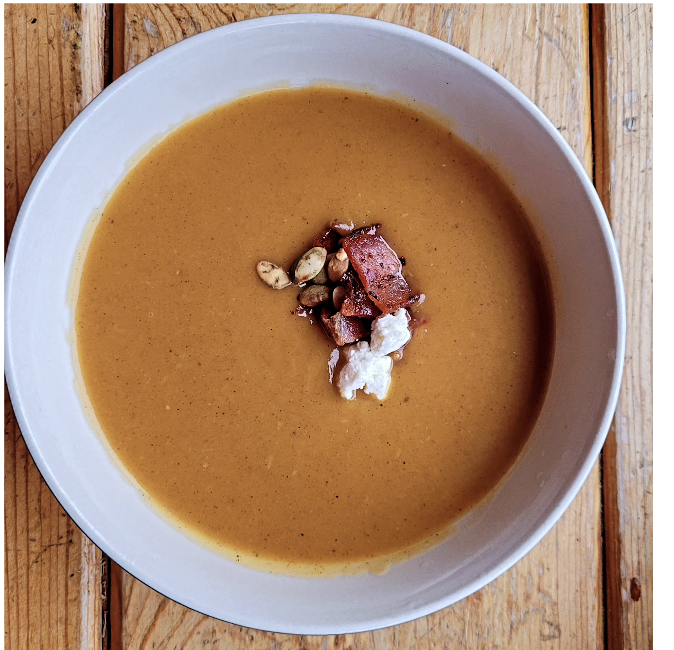 squash soup in a white bowl dressed with nuts and bacon