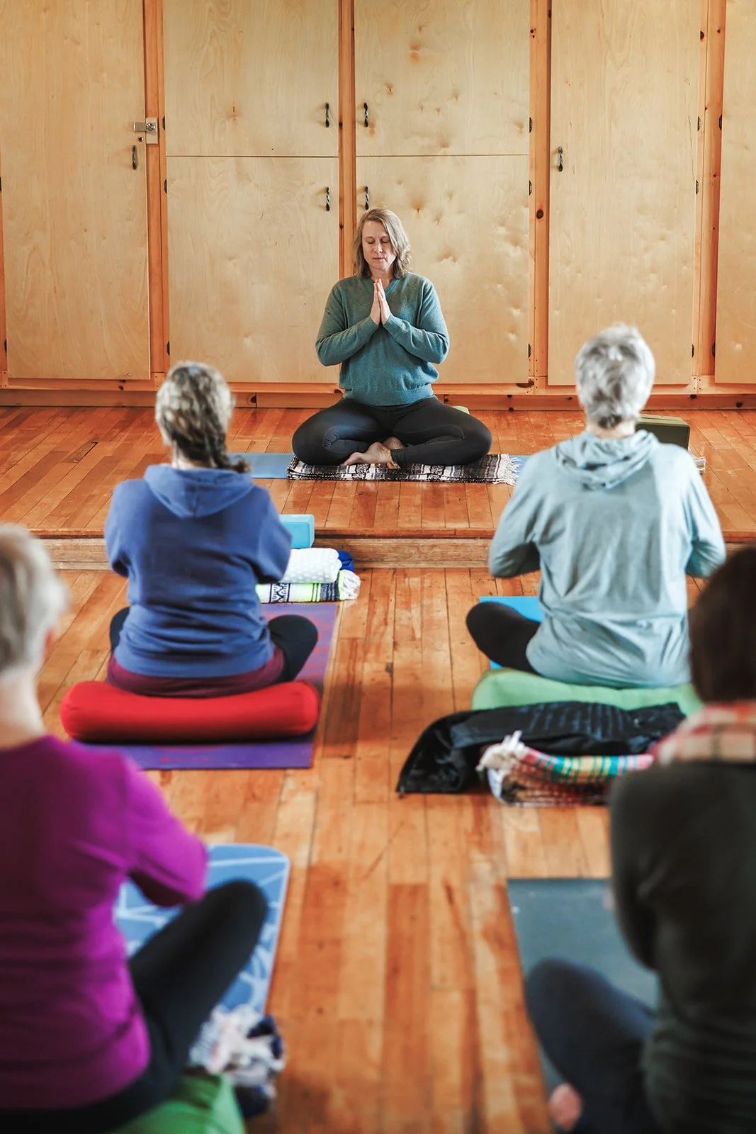 yoga teacher at front of class seated with rest of class
