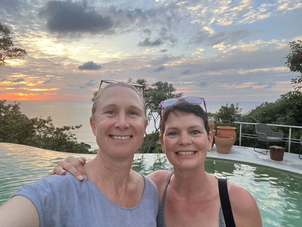 two women joanna dunn yoga and sam switzer chef looking at camera with sunset and swimming pool in the background