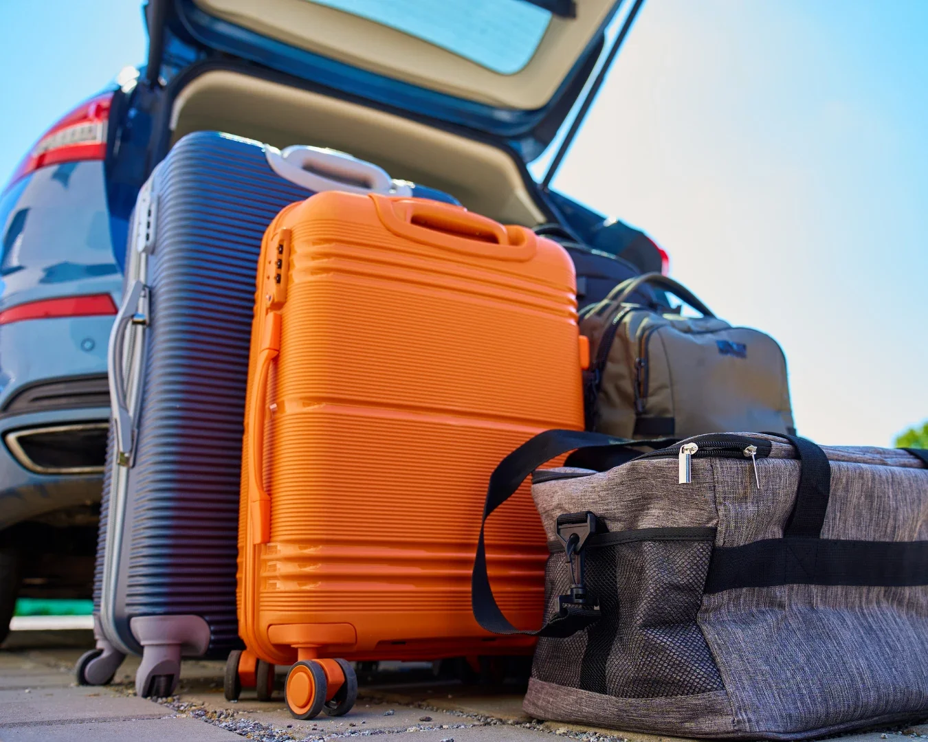 A pile of luggage on the ground next to an open car trunk