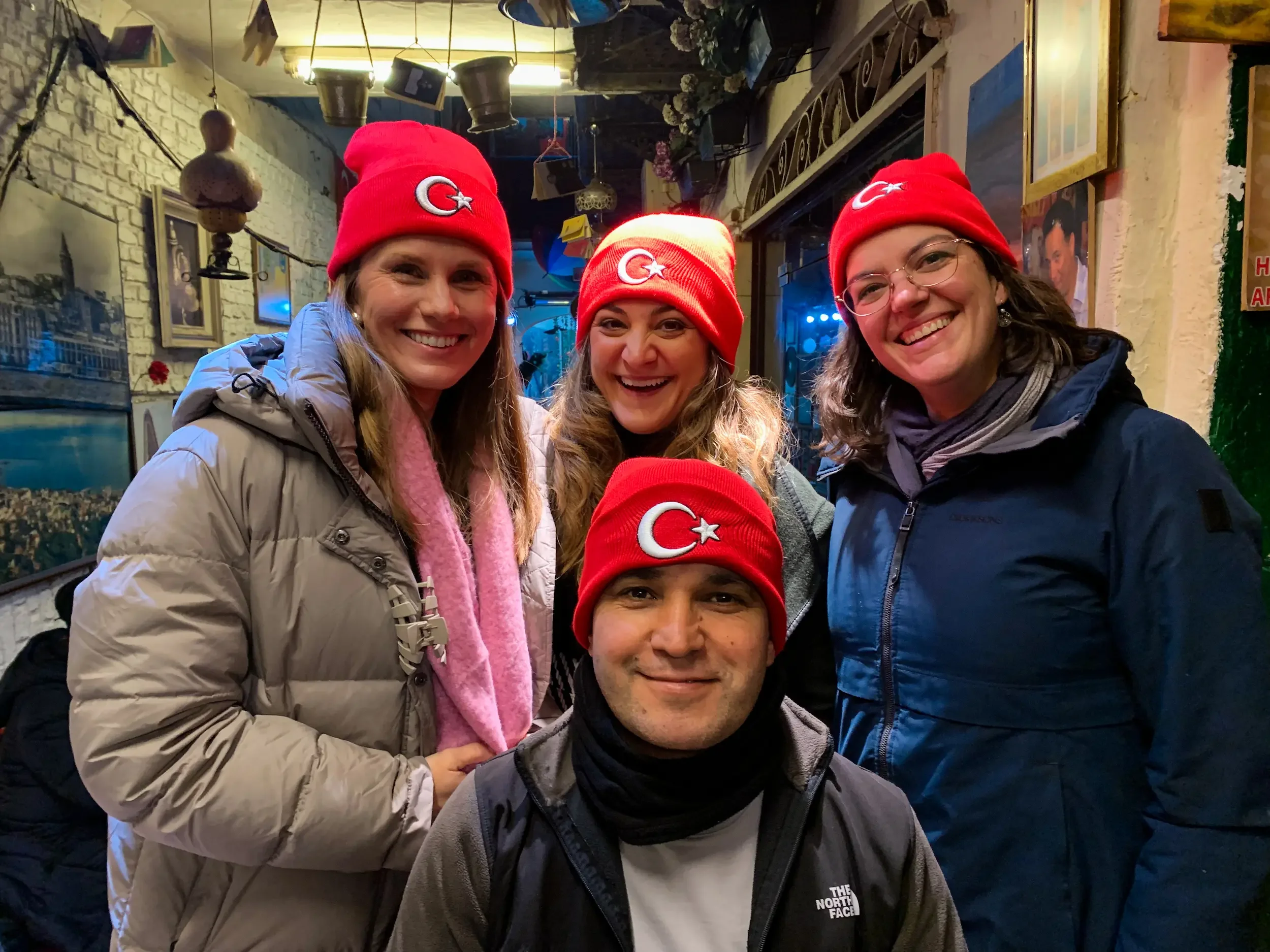 Three women on a food tour in Istanbul wearing red Turkey hats with the owner of a tea shop in Istanbul