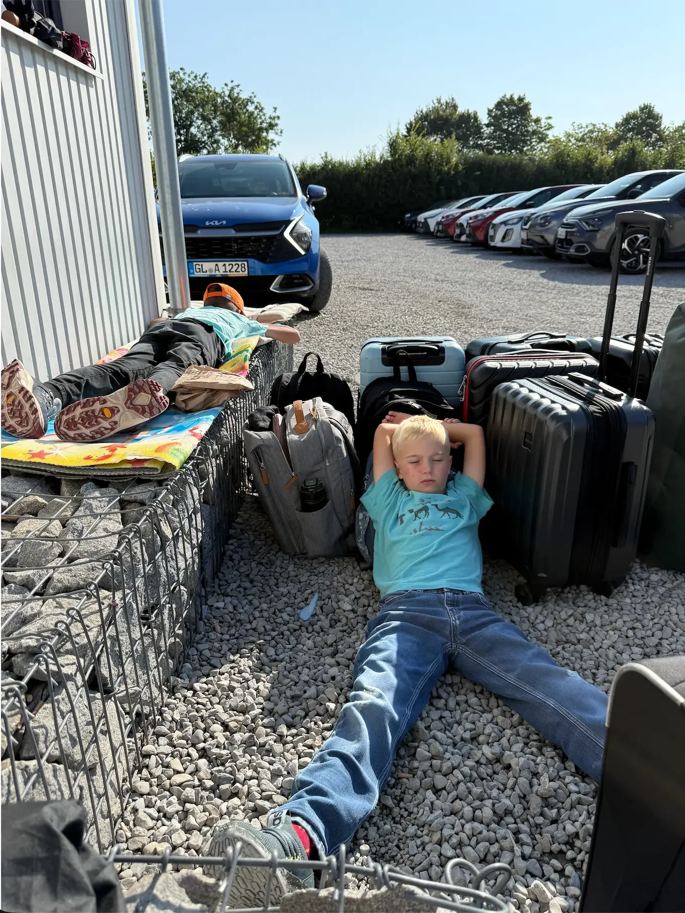 Kids laying down exhausted next to a lot of luggage at a rental car pickup point