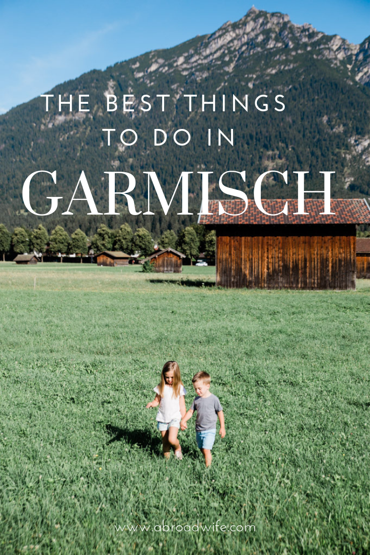 Two children walking in grass field below mountains in Germany. Text overlay “The Best things to Do in Garmisch”