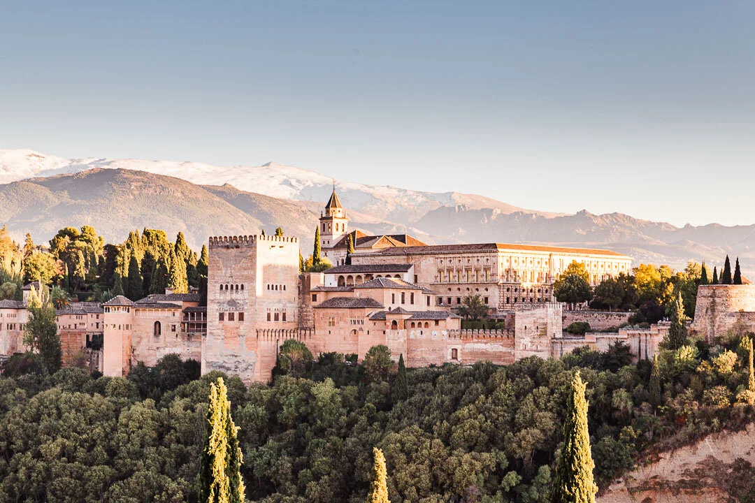 Sunset view of the entire Alhambra complex with snowcapped Sierra Nevada mountains in the background.