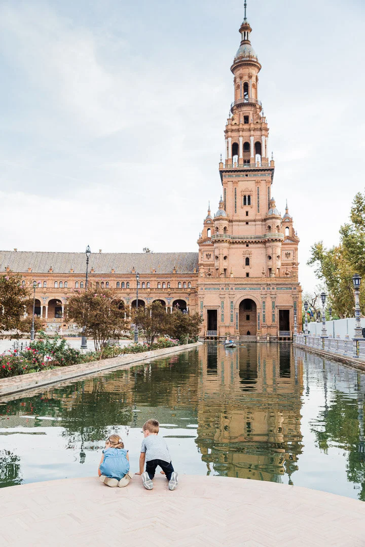 Kids kneeling down to look for fish in the canals of the Plaza de España in Seville, Spain.