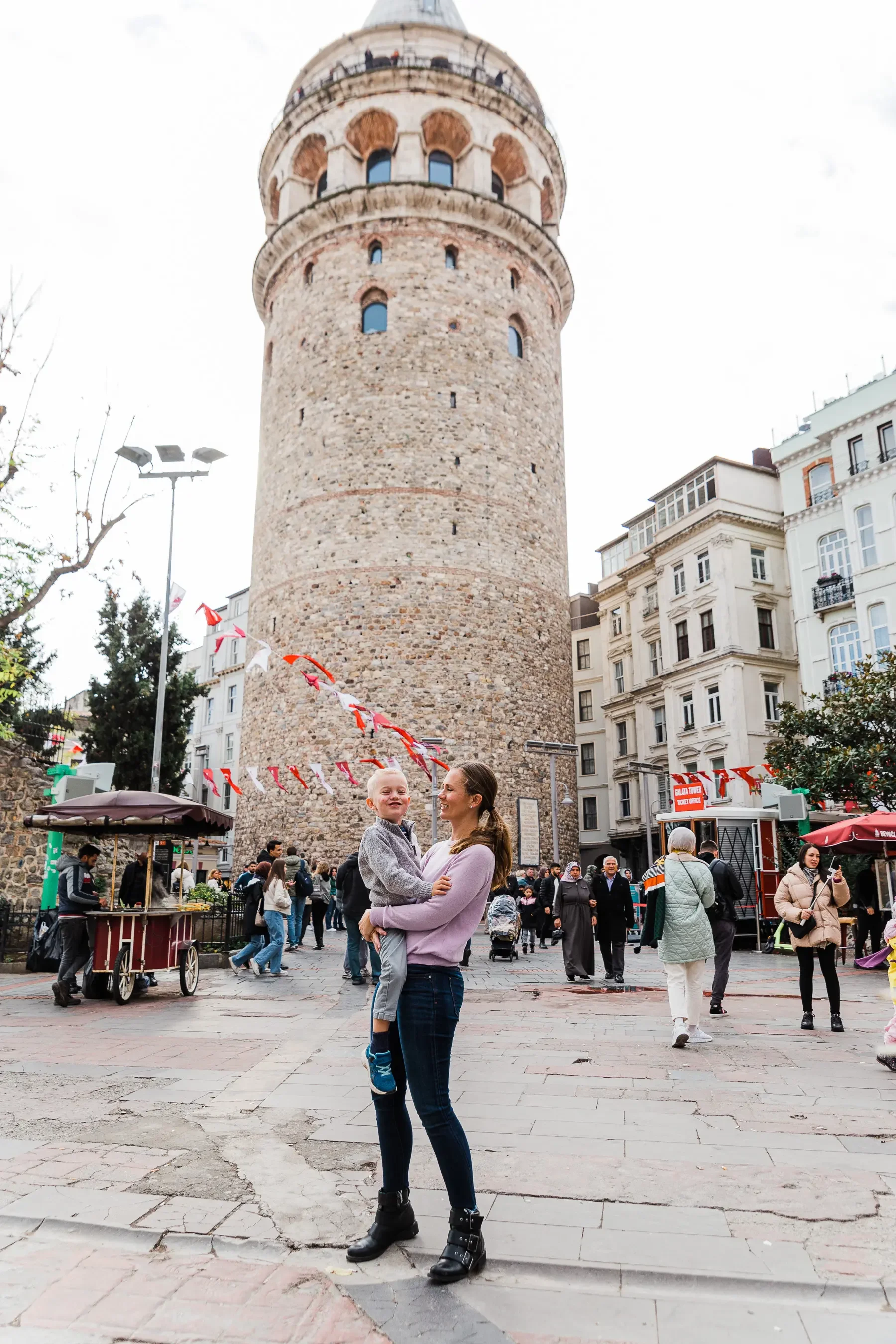 Woman holding a toddler standing in front of the Galata Tower in Istanbul