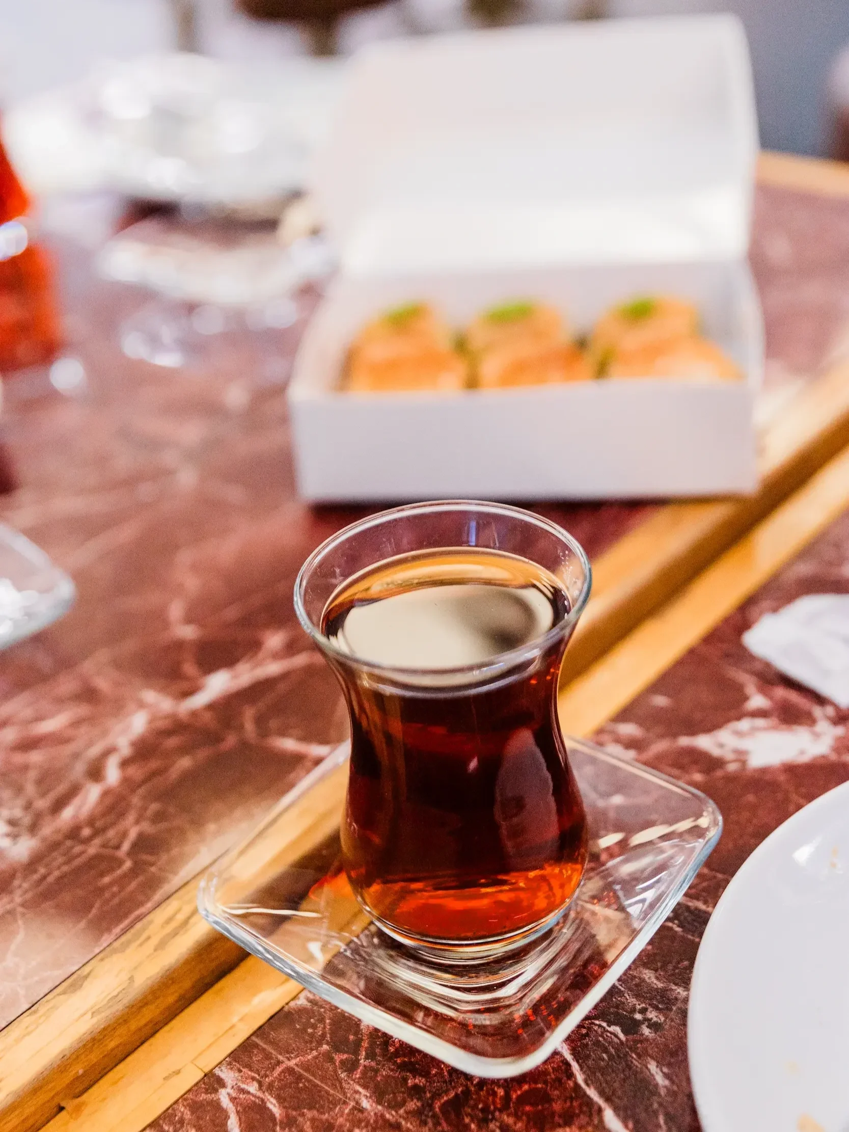 Turkish tea in tulip glass on a table with a box of baklava in the background on an Istanbul food tour.