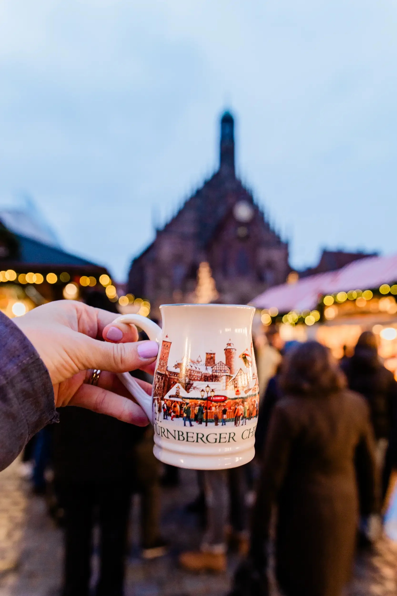 Woman's hand holding a Nuremberg Christmas market mug with the Christmas market int he background